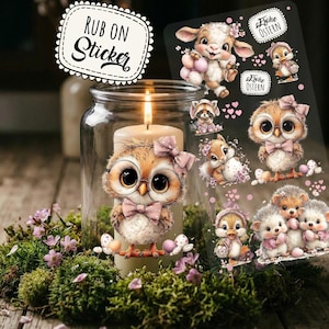 Könnte beinhalten: Eine brennende Kerze in einem Glas, umgeben von Moos und Blumen, mit einem Aufkleber mit der Aufschrift "RUB ON Sticker". Ein Bogen mit Aufklebern zum Thema Ostern zeigt niedliche Tierillustrationen, darunter eine Eule, ein Lamm und ein Igel, mit dem Text "Frohe Ostern".