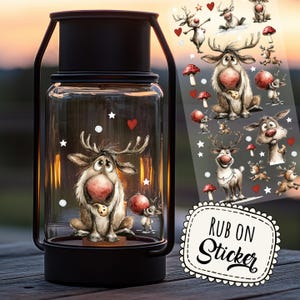 May include: A black metal lantern with a clear glass jar featuring a reindeer illustration. The jar is decorated with white stars and red heart stickers. A sheet of reindeer stickers is visible to the right. The words "RUB ON Sticker" are on a white label.