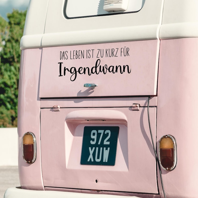 May include: A pink vintage van with a black sticker that reads "Das Leben ist zu kurz f&uuml;r Irgendwann". The van has a license plate that reads "972 XUW".