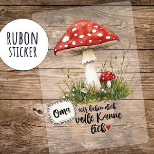 May include: A clear sticker featuring a watercolor illustration of a red mushroom with white spots, surrounded by grass and daisies. The sticker includes the text "Oma wir haben dich volle Kanne lieb" and "RUBON STICKER".