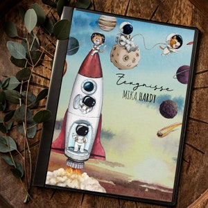 Op de afbeelding: Een blauwe en witte raket met een katten-astronaut en een ruimtevaarder-astronaut die door de ruimte vliegen. De raket is omringd door planeten en sterren. De tekst "Zeugnisse Mika Hardy" staat op de raket.