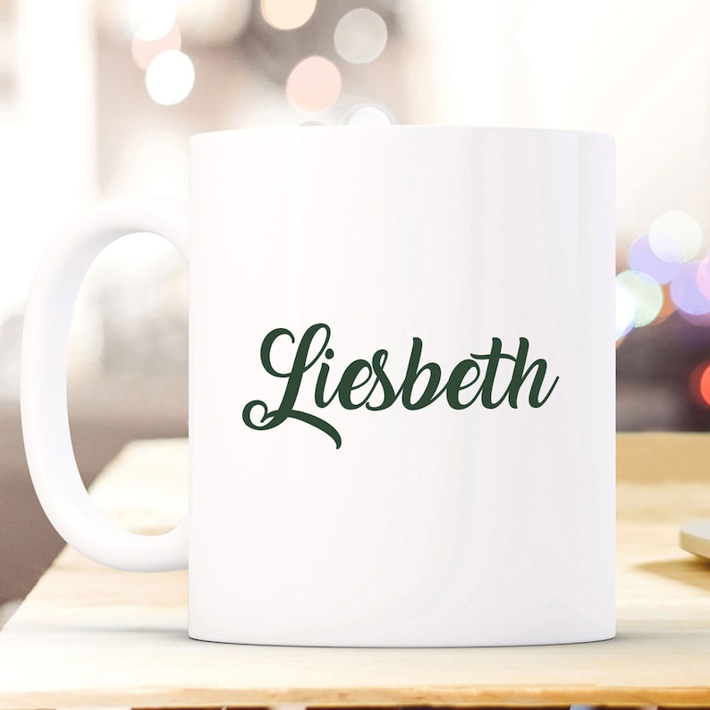 May include: White ceramic coffee mug with a green cursive name "Liesbeth" printed on the front.
