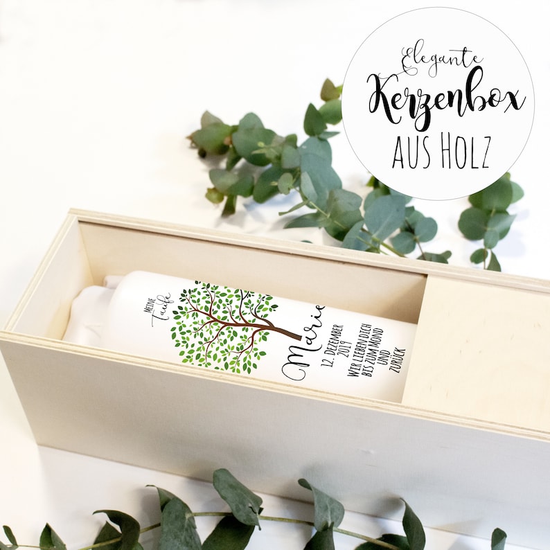 May include: A white wooden box with a white label that says "MEINE Taufe Marie 12. DEZEMBER 2019 WIR LIEBEN DICH BIS ZUM MOND UND ZUR&Uuml;CK". The box is decorated with a green tree illustration. The box is labeled "Elegante Kerzenbox AUS HOLZ".