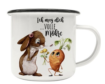 May include: White enamel mug with a black rim and handle. The mug features a cartoon illustration of a rabbit holding a bouquet of yellow flowers and a carrot with a face and arms holding a single yellow flower. The text on the mug reads "Ich mag dich...volle Möhre".