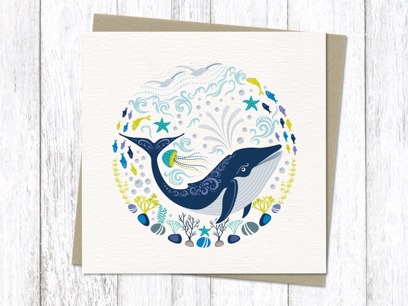 Colourful Blue whale greeting card in our circular Nordic folk art style. It features a whale in deep blue, followed by a shoal of little fishes , pebbles, coral and jelly fish in bright contemporary coastal colours.