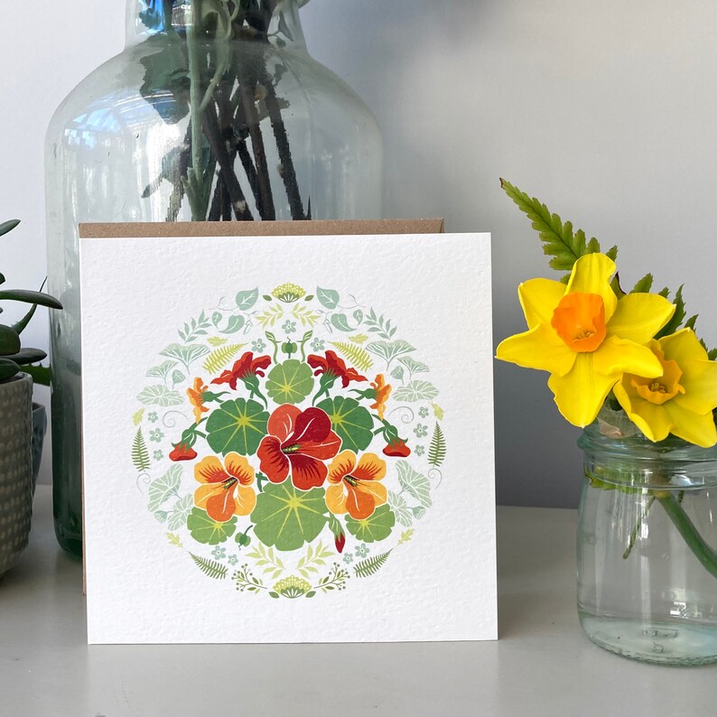 Nasturtium greeting card on a shelf with a little jug of daffodils to the right.