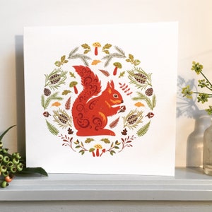 Red Squirrel Card shown on a shelf with berries and a vase of flowers.