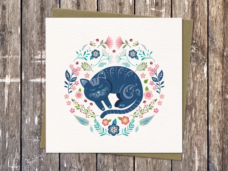 Colourful Cat illustration in my circular Nordic folk art style. It features a sleeping cat surrounded by flowers, ferns and leaves in  blues, pinks and turquoise. Square Card with Brown Eco Envelope.