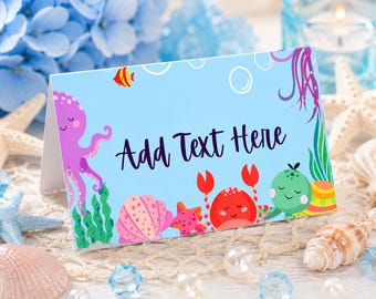 May include: A light blue folded card featuring the text Add Text Here in dark purple script. The design includes a purple octopus, a red crab, a pink seashell, a small orange fish, green seaweed, and white bubbles on a light blue background.