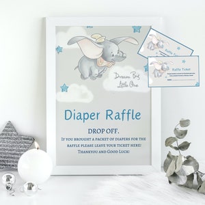 Puede incluir: Un cartel enmarcado en blanco con una ilustración azul y gris de Dumbo el elefante volando con un fondo de estrellas azules y nubes. El cartel dice "Dream Big Little One" y "Diaper Raffle". El texto debajo dice "Drop Off. If you brought a packet of diapers for the raffle please leave your ticket here! Thank you and good luck!"
