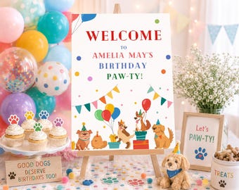 May include: A white rectangular birthday sign on a wooden easel featuring the text WELCOME TO AMELIA MAY'S BIRTHDAY PAW-TY! decorated with colorful illustrations of dogs wearing party hats, balloons, and bunting flags against a white background.