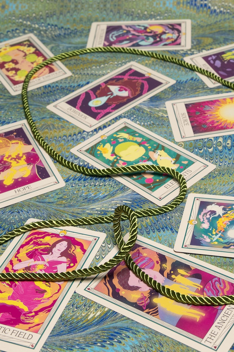 May include: A collection of tarot cards with colorful illustrations and text, arranged on a patterned surface. A green and gold rope is looped around some of the cards. The cards feature images of figures, planets, and abstract designs.