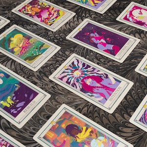May include: A collection of tarot cards with colorful, abstract illustrations. Each card features a unique design with vibrant hues of purple, pink, yellow, and green. The cards are arranged on a patterned surface, showcasing the intricate artwork.