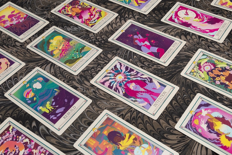 May include: A collection of tarot cards with colorful, abstract illustrations. Each card features a unique design with vibrant hues of purple, pink, yellow, and green. The cards are arranged on a patterned surface, showcasing the intricate artwork.