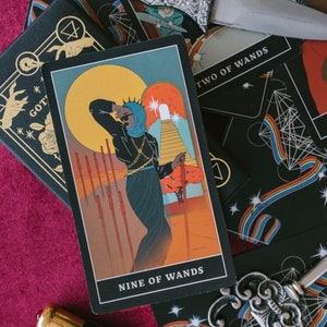 May include: A Nine of Wands tarot card featuring a figure in a black outfit and blue head covering, surrounded by eight wands, with a large yellow sun and a staircase in the background. A silver dagger and an ornate silver key rest on the cards.