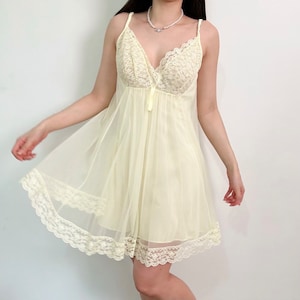 May include: A pale yellow lace slip dress with a V-neckline and delicate lace trim. The dress is made of a sheer fabric and has a flowy silhouette.