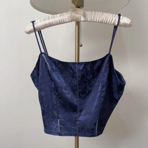 May include: A navy blue satin top with a floral pattern and a lace trim. The top has thin straps and a cropped fit.