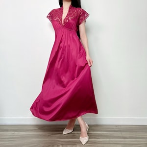 May include: A floor-length magenta nightgown featuring a V-neckline with intricate lace detailing on the bodice and short sleeves. The garment has a high-waisted empire silhouette with a flowing, smooth skirt that extends to the ankles.