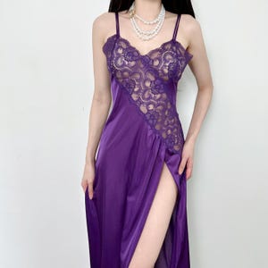 May include: A vibrant purple satin slip dress with delicate lace detailing on the bodice and a high slit. The dress features thin spaghetti straps and a flowing silhouette, perfect for a special occasion.