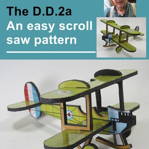 May include: A green and white model airplane with a red, white, and blue tail. The model is a D.D.2a, an easy scroll saw pattern. The model is on a white background.