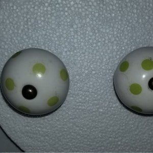 Puede incluir: Dos pomos de cerámica blanca con lunares verdes y un centro negro.