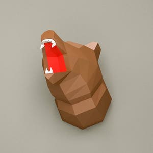 May include: A brown papercraft bear head with an open mouth and white teeth. The bear's mouth is red.