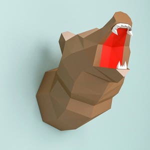 May include: A papercraft model of a bear's head with an open mouth, showing sharp teeth and a red tongue. The model is made of brown paper and is mounted on a wall.