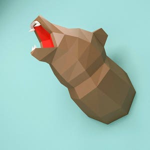 May include: A brown papercraft bear head with an open mouth and red paper inside. The bear head is mounted on a light blue wall.
