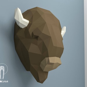 May include: A brown papercraft bison head with white horns. The bison head is a 3D model and is made of paper.
