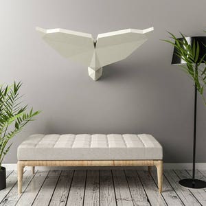 Pode incluir: Escultura de parede de baleia de origami branca pendurada em uma parede cinza com um banco de madeira e duas plantas em vasos em primeiro plano.
