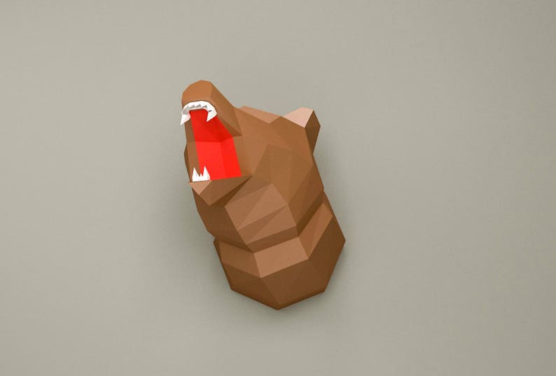 May include: A brown papercraft bear head with an open mouth and white teeth. The bear's mouth is red.