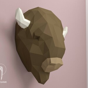 May include: A brown papercraft bison head with white horns. The bison head is a 3D model and is made of folded paper.