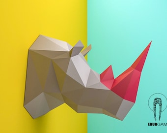 May include: A gray papercraft rhinoceros head with a red horn, mounted on a yellow and blue background. The rhinoceros is made of folded paper and has a geometric design. The background is a split color, with yellow on the left and blue on the right.