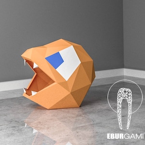 May include: A 3D paper model of a Pac-Man character with an open mouth, made of orange paper with a blue and white eye.