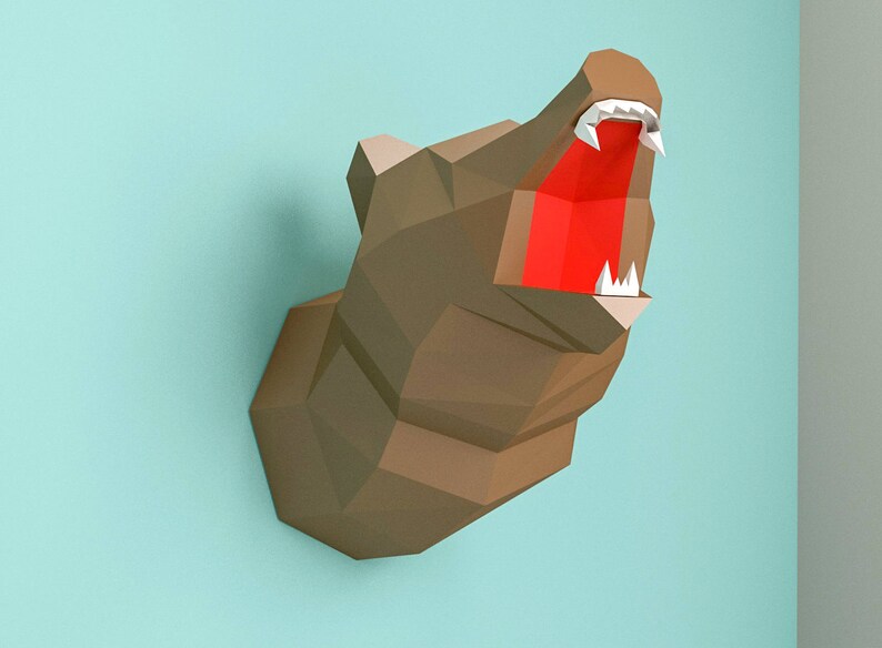 May include: A papercraft bear head with a brown fur texture and an open mouth with red inside and white teeth. The bear head is mounted on a light blue wall.