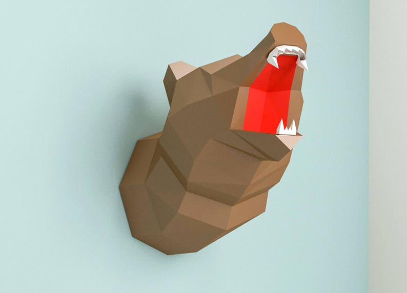 May include: A papercraft model of a bear's head with an open mouth, showing sharp teeth and a red tongue. The model is made of brown paper and is mounted on a wall.