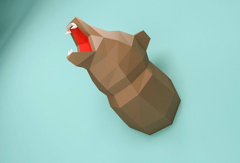 May include: A brown papercraft bear head with an open mouth and red paper inside. The bear head is mounted on a light blue wall.