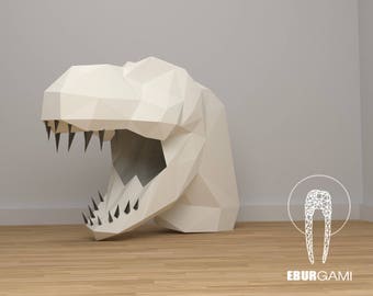 May include: A white papercraft dinosaur head with a large open mouth and sharp teeth. The dinosaur head is made of folded paper and has a 3D effect. The background is a light gray wall with a wooden floor.