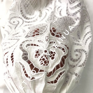 May include: White cotton fabric with a delicate lace pattern. The lace is cut out, creating a see-through effect. The fabric is gathered at the bottom, creating a ruffled look.