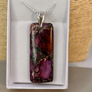 May include: A silver chain necklace with a rectangular pendant featuring a purple and brown stone with a marbled pattern.