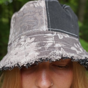 May include: A gray and black bucket hat with a floral pattern and frayed edges. The hat is made of a soft, comfortable fabric.