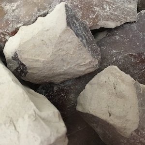 May include: Close-up of a pile of white and brown clay rocks. The rocks are rough and have a natural, earthy texture.