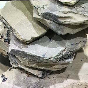 Könnte beinhalten: Ein Stapel Schieferplatten in verschiedenen Grautönen und Braun. Die Platten sind übereinander gestapelt und erzeugen einen natürlichen und rustikalen Look.