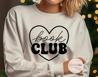 Könnte beinhalten: Weißes Sweatshirt mit einem schwarzen herzförmigen Aufdruck, der "book CLUB" in einer Kombination aus Schrift und fetten Blockbuchstaben zeigt. Das Sweatshirt ist ein langärmeliges Rundhals-Sweatshirt.