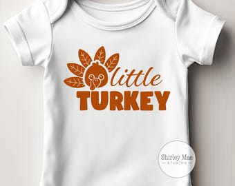 Puede incluir: Un body blanco para bebé con un gráfico de pavo marrón y el texto "little turkey".