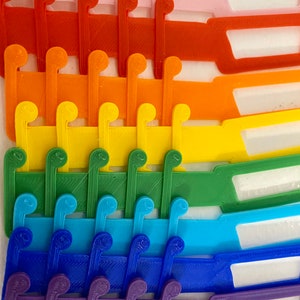 May include: A set of colorful plastic organizers with a series of hooks on each piece. The organizers are stacked in a rainbow pattern, starting with pink and ending with brown.