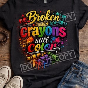 May include: A black short-sleeved t-shirt featuring a graphic print with the text "Broken crayons still colour" in multi-coloured, paint-splattered lettering. The design includes illustrations of various broken crayons in red, yellow, blue, and green.