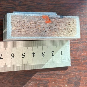 Pu&ograve; includere: Primo piano di un blocco di legno con una cornice in metallo grigio. Il blocco &egrave; largo circa 2,5 cm e lungo 7,5 cm. Il legno ha una venatura naturale ed &egrave; leggermente rovinato.