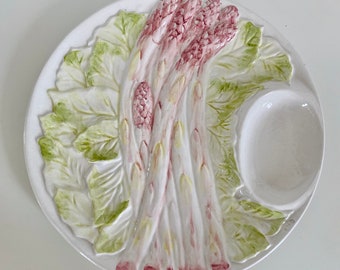 May include: White ceramic serving dish with a raised design of asparagus and leaves. The dish has a small, round dip bowl.