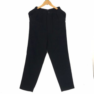 Peut inclure: Pantalon noir suspendu à un cintre en bois. Le pantalon a une fermeture boutonnée et des plis à la taille. Les jambes sont droites et le tissu semble être d'épaisseur moyenne.